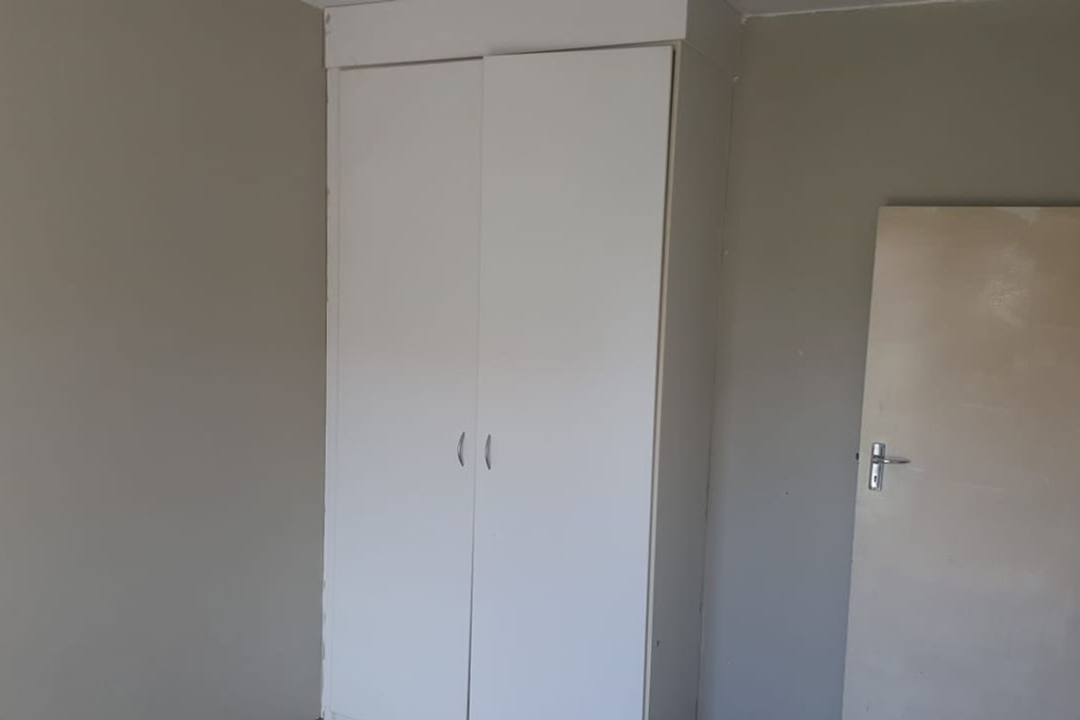 A simple bedroom interior featuring a built-in white wardrobe and a standard interior door, requiring minor cosmetic updates to the walls and paintwork.