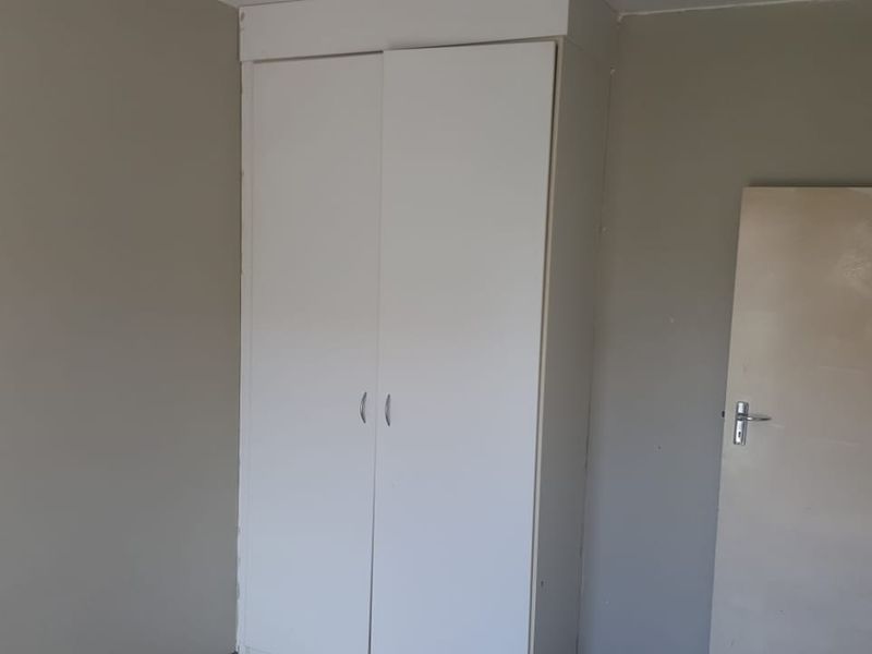 A simple bedroom interior featuring a built-in white wardrobe and a standard interior door, requiring minor cosmetic updates to the walls and paintwork.