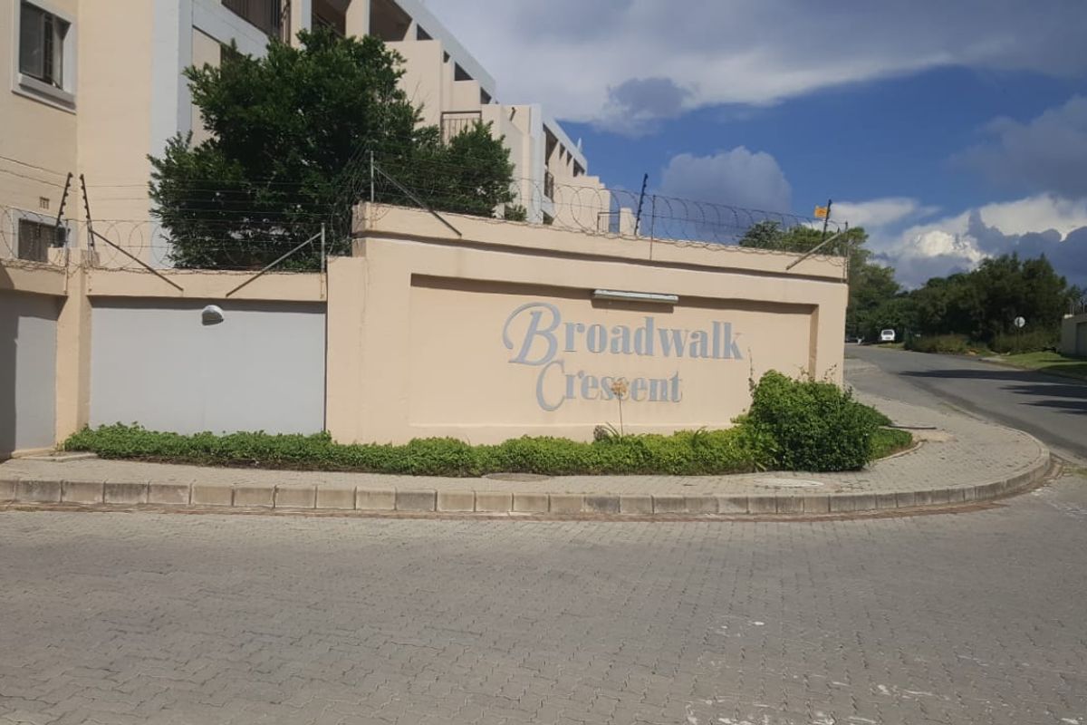 Street view of the Broadwalk Crescent complex entrance, featuring a perimeter wall with electric fencing and paved sidewalk access.