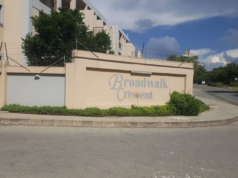 Street view of the Broadwalk Crescent complex entrance, featuring a perimeter wall with electric fencing and paved sidewalk access.