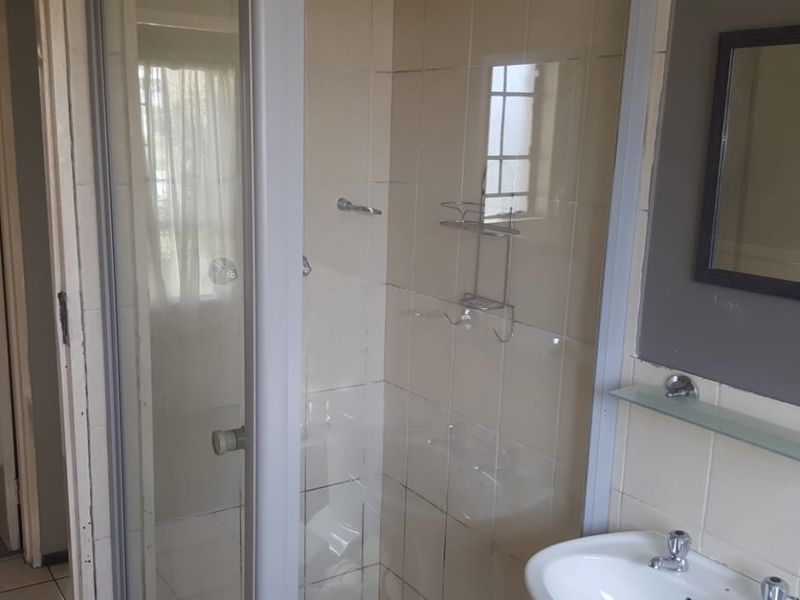 A functional bathroom featuring a shower enclosure, pedestal basin, and tiled finishes, offering a blank canvas for potential modernization and cosmetic updates.