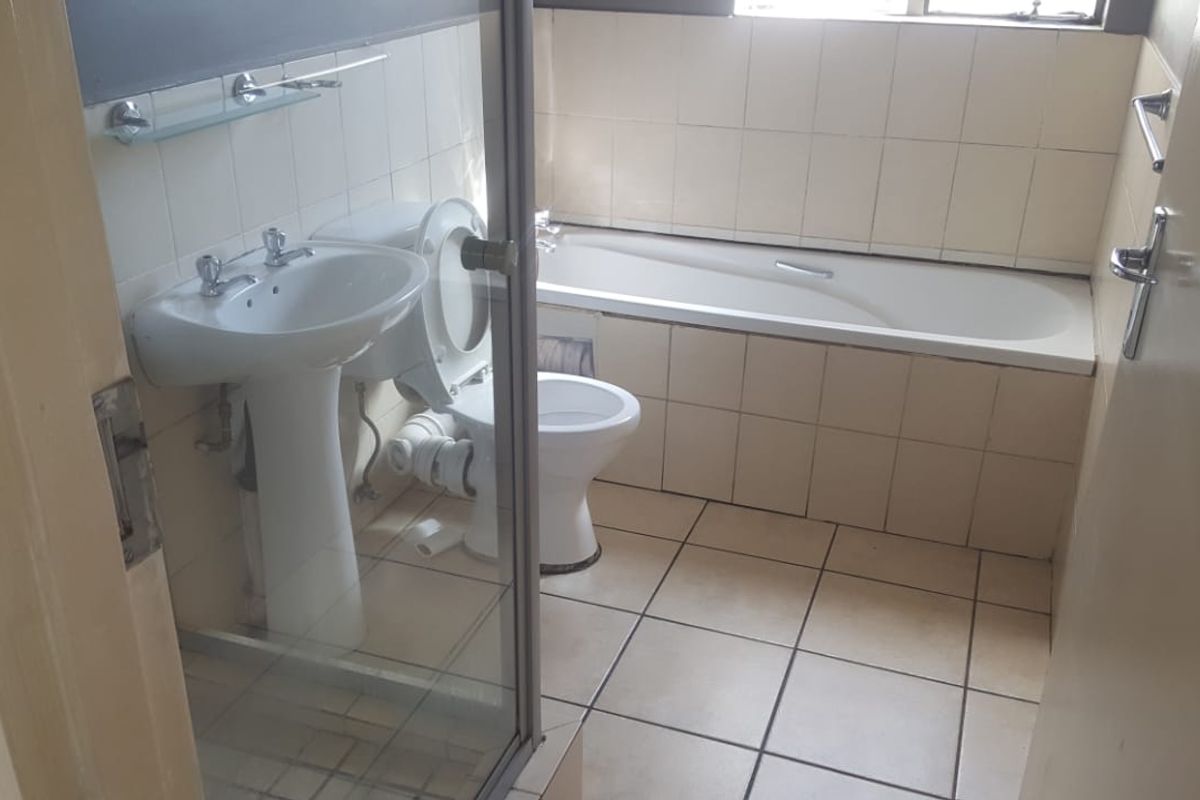 A functional bathroom featuring a pedestal basin, toilet, and built-in bathtub with tiled finishes, requiring some cosmetic updates.