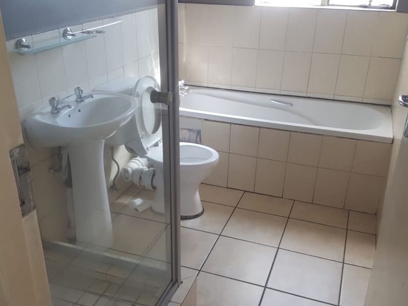 A functional bathroom featuring a pedestal basin, toilet, and built-in bathtub with tiled finishes, requiring some cosmetic updates.