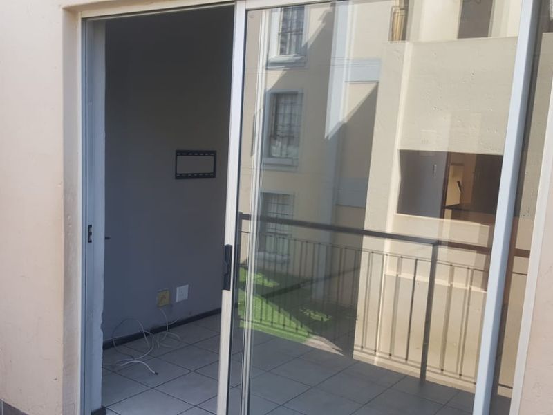 A view from a balcony looking into an empty room, featuring tiled flooring, a sliding glass door, and a metal balustrade.