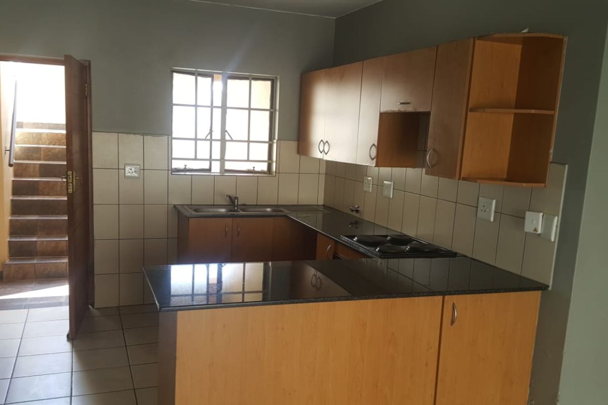A functional kitchen featuring built-in wooden cabinetry, granite countertops, an electric hob, and tiled finishes, with direct access to an external staircase.