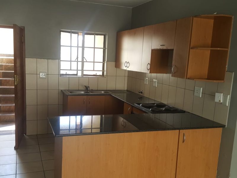 A functional kitchen featuring built-in wooden cabinetry, granite countertops, an electric hob, and tiled finishes, with direct access to an external staircase.