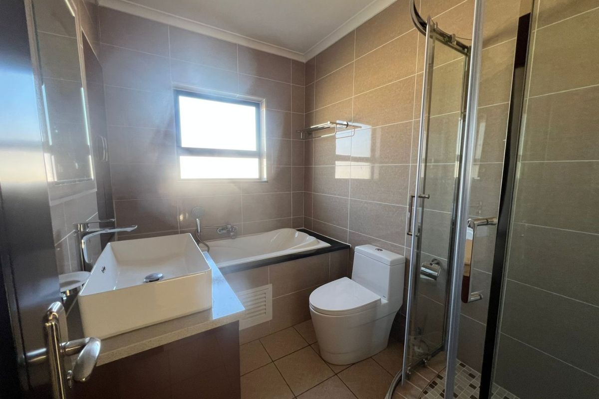 Modern bathroom featuring a vessel sink vanity, built-in bathtub, separate shower enclosure, and neutral floor-to-ceiling wall tiling.