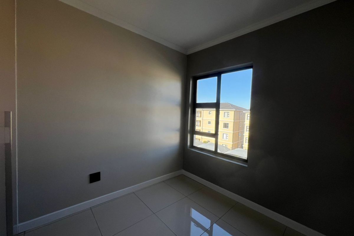 A bright, empty bedroom featuring neutral painted walls, modern tiled flooring, and an aluminium-framed window providing natural light.