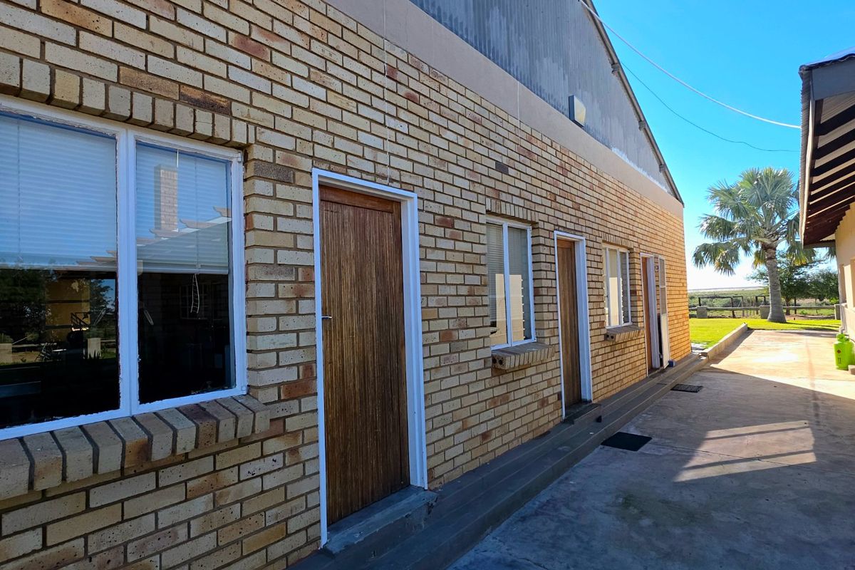 Exterior view of a face brick farm building featuring multiple access doors and aluminium windows with a concrete walkway.