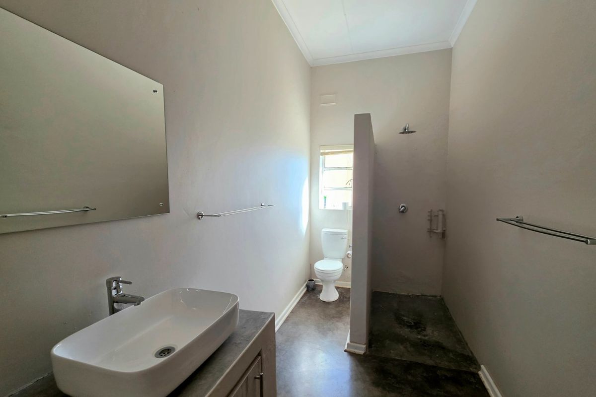 A minimalist bathroom featuring a vessel sink vanity, a walk-in shower area, and a separate toilet, finished with concrete flooring.