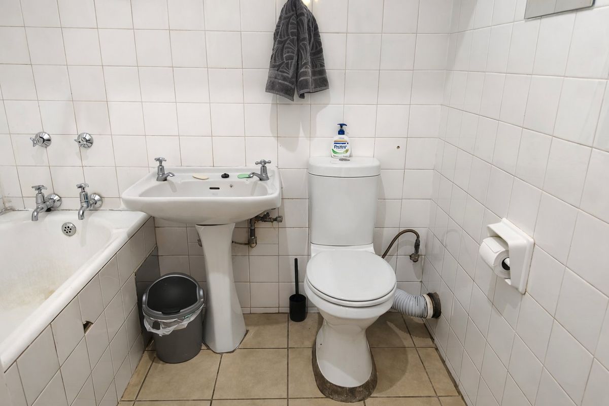 A compact bathroom featuring a pedestal basin, standard toilet, and bathtub with wall-mounted taps, finished with white wall tiles.