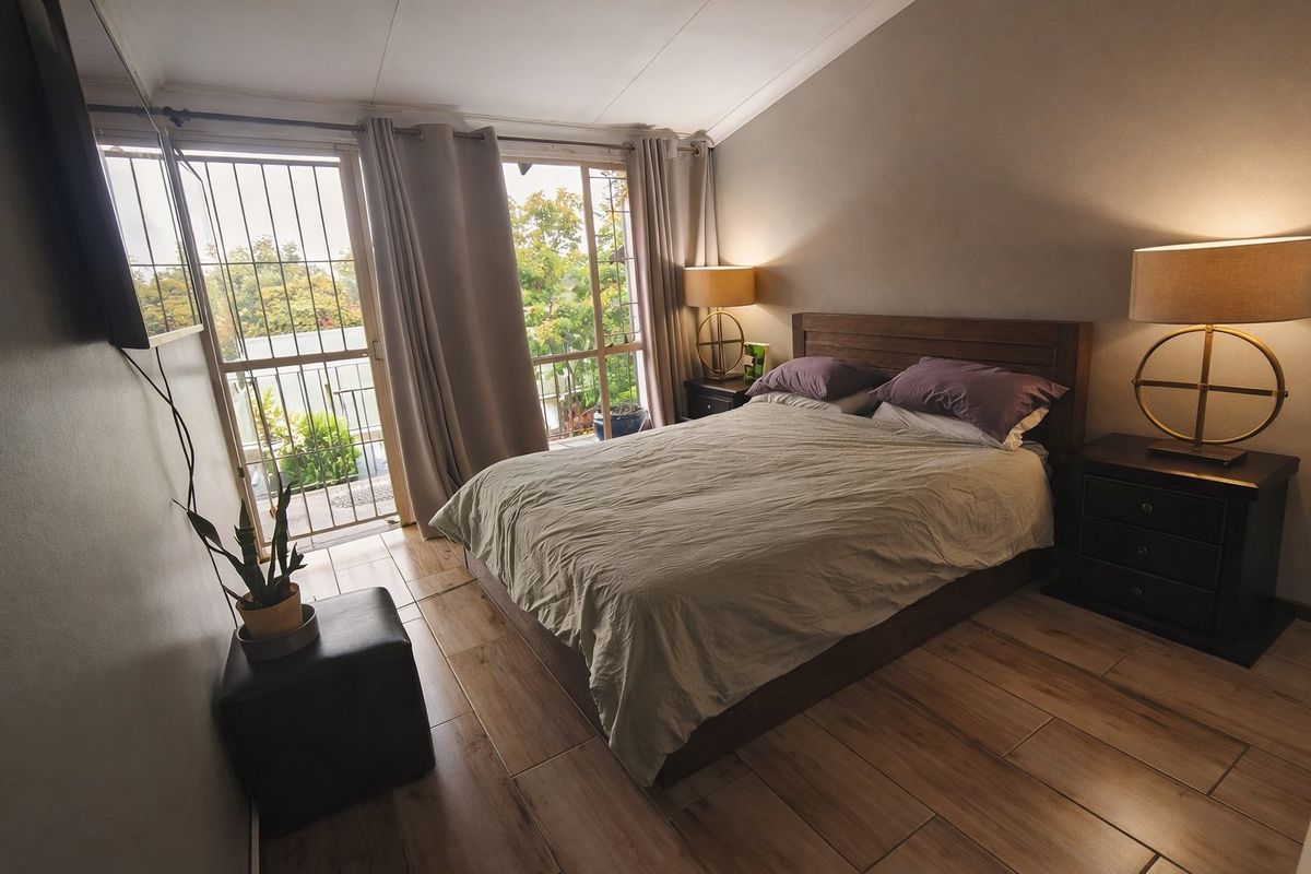 A well-lit bedroom featuring wood-look tile flooring and a sliding glass door with security gate leading to a private balcony.