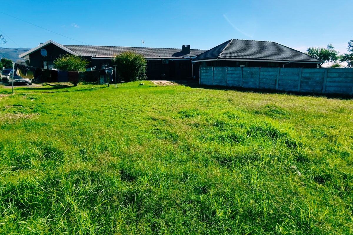 A spacious rear garden area featuring a large lawn, enclosed by precast concrete boundary walls, with a view of the rear building elevation.