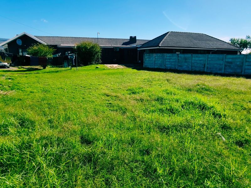 A spacious rear garden area featuring a large lawn, enclosed by precast concrete boundary walls, with a view of the rear building elevation.