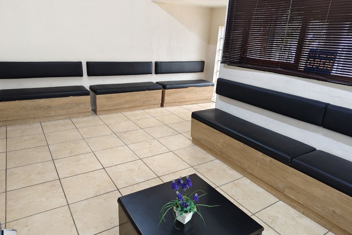 A commercial waiting area featuring built-in bench seating with wood-look bases, ceramic tiled flooring, and dark venetian blinds.