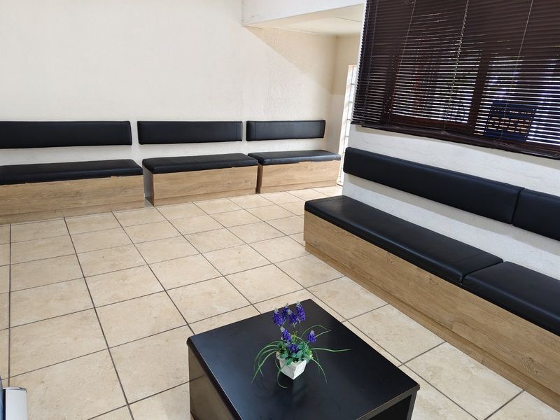 A commercial waiting area featuring built-in bench seating with wood-look bases, ceramic tiled flooring, and dark venetian blinds.
