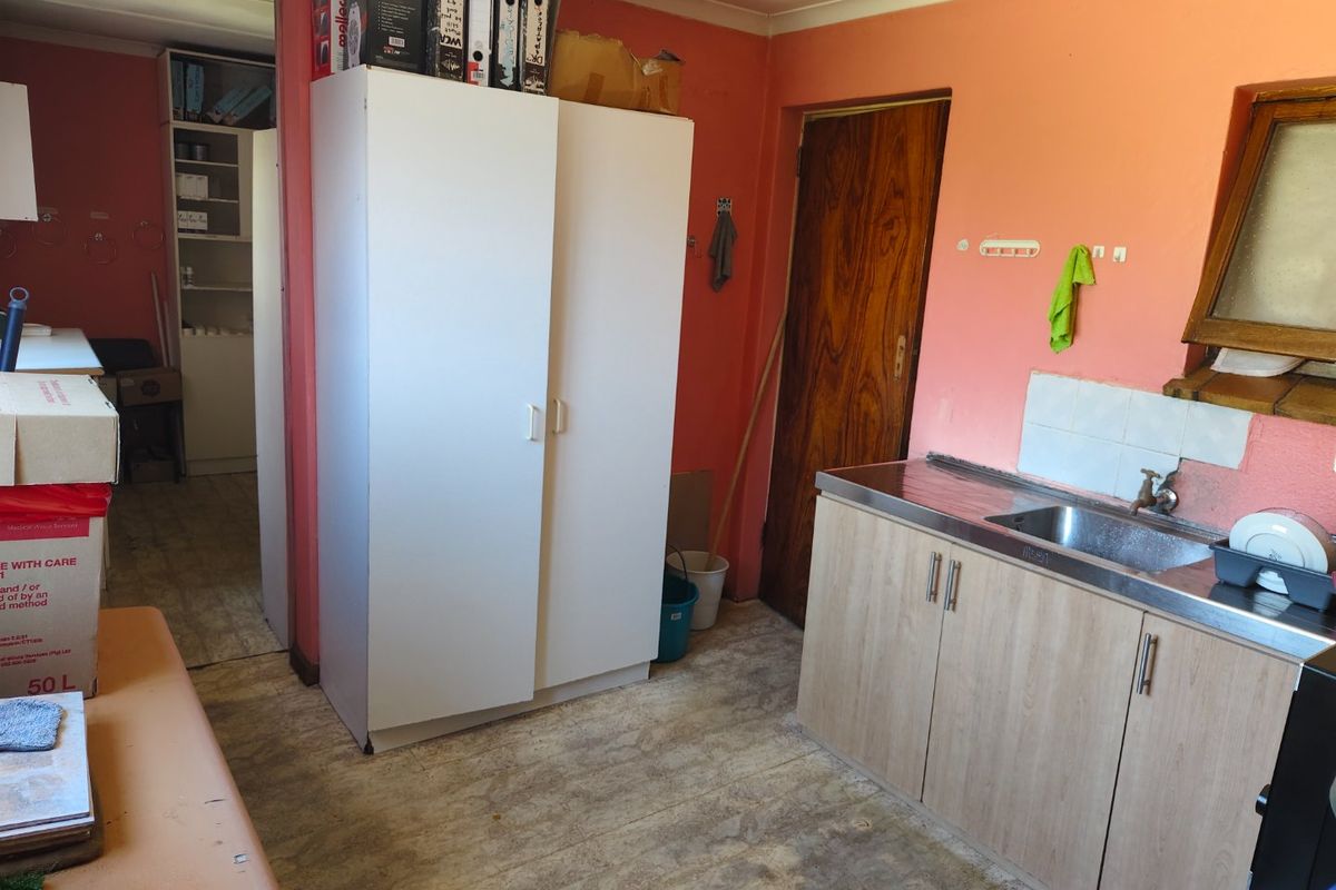 A functional kitchen area featuring a stainless steel sink, built-in cabinetry, and tiled splashback, currently used as a utility and storage space.