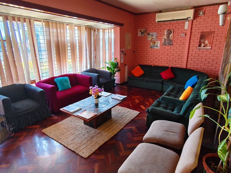 A spacious living area featuring classic parquet flooring, an exposed brick feature wall, and a wall-mounted air conditioning unit.
