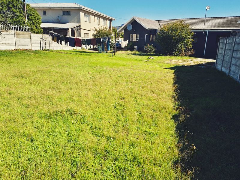 A spacious rear garden area featuring a large lawn, enclosed by precast concrete boundary walls, with views of the rear building elevation.