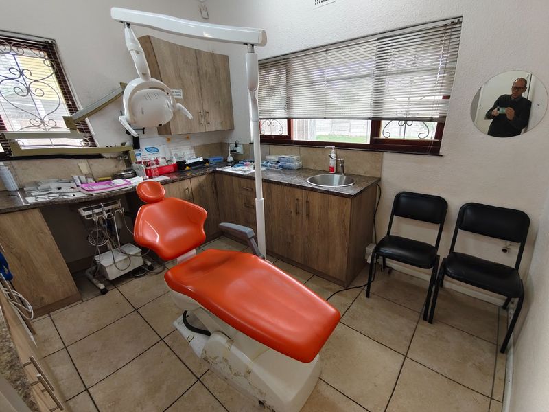 A functional dental examination room featuring built-in cabinetry, a stainless steel sink, tiled flooring, and professional dental equipment.