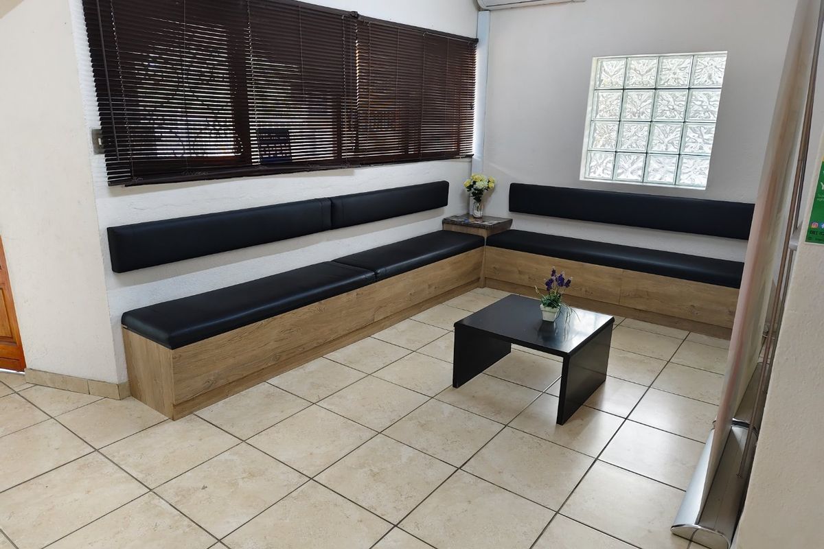 A commercial waiting area featuring built-in bench seating, ceramic floor tiles, a glass block window, and a wall-mounted air conditioning unit.