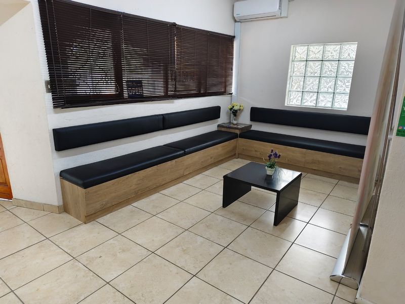 A commercial waiting area featuring built-in bench seating, ceramic floor tiles, a glass block window, and a wall-mounted air conditioning unit.