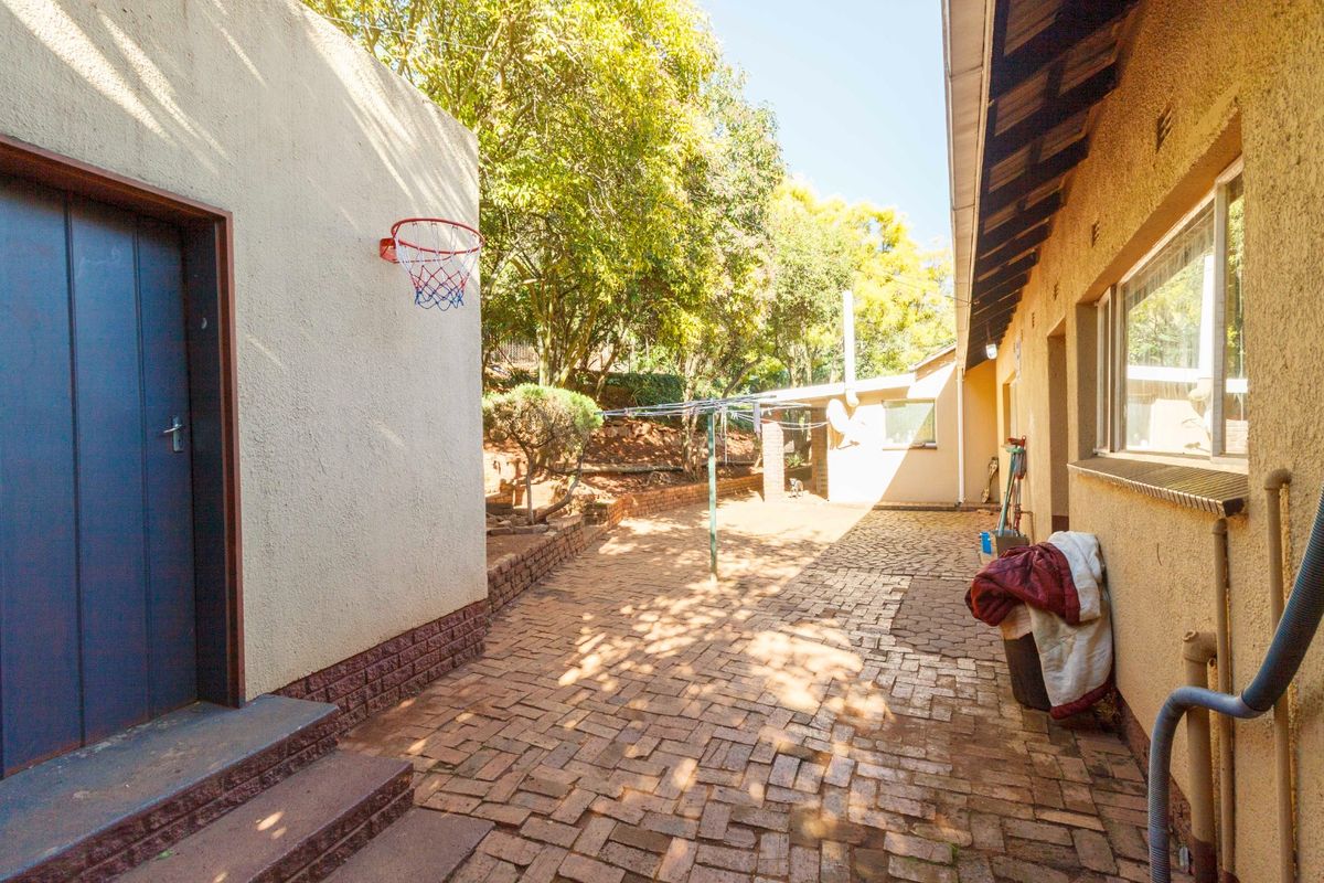A paved rear courtyard area featuring a retaining wall, mature trees, and access to the main dwelling and outbuilding.