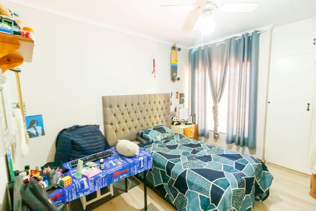 A functional bedroom featuring laminate flooring, a ceiling fan, and a built-in cupboard, providing a comfortable and practical living space.
