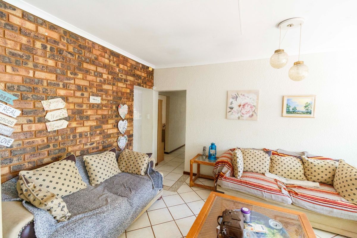 A living room featuring an exposed brick accent wall, ceramic floor tiles, and pendant lighting, offering a cozy and traditional living space.