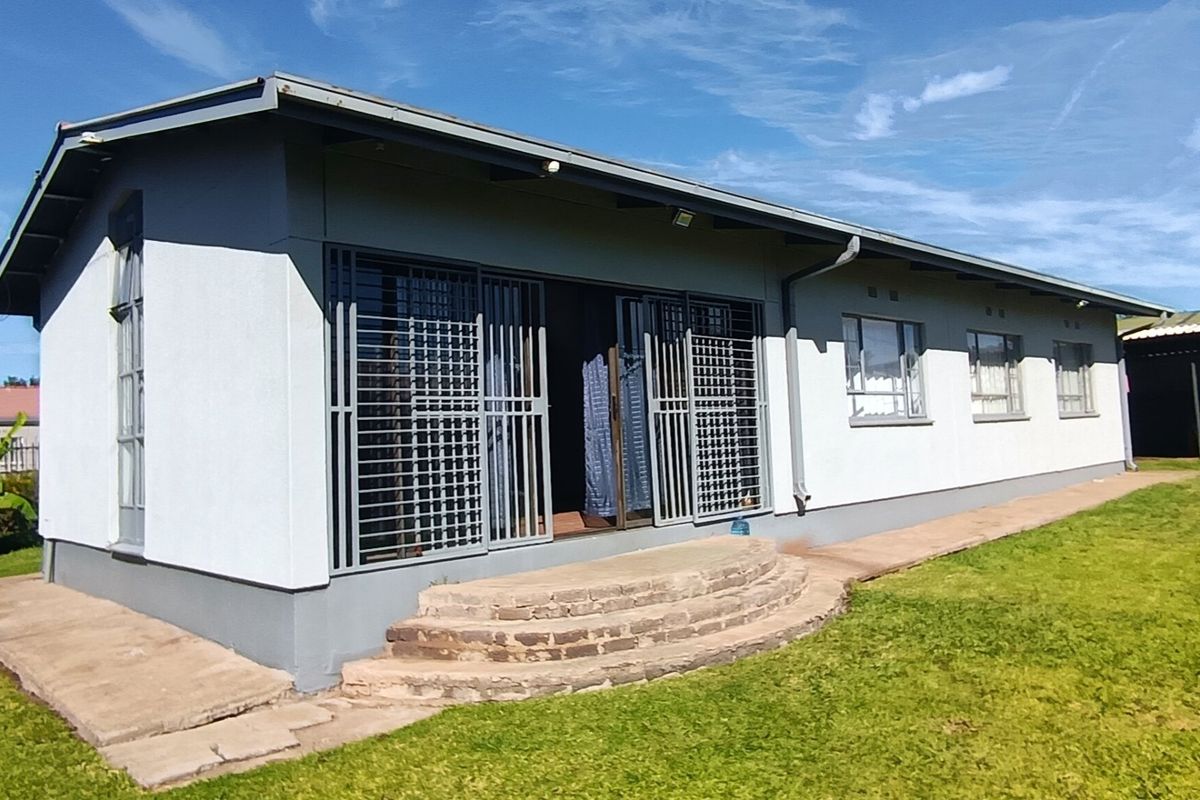 Rear view of the house featuring a lawn, stone steps leading to sliding doors with metal security gates, and functional guttering.