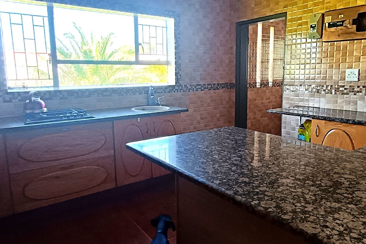 A functional kitchen featuring granite countertops, built-in hob, and tiled splashbacks, offering a practical layout with ample storage space.