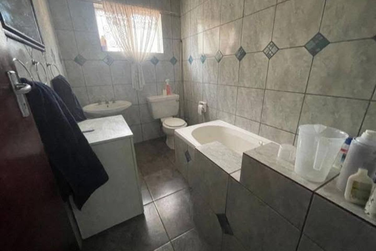 A dated bathroom featuring a built-in bathtub, pedestal sink, and toilet, finished with full-height wall tiling and floor tiles.