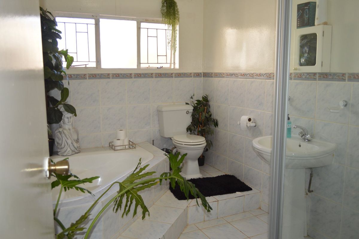 A dated bathroom featuring a built-in corner bathtub, pedestal sink, and toilet with tiled finishes throughout.
