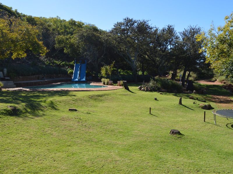 Spacious outdoor area featuring a swimming pool with a slide, surrounded by landscaped gardens and mature trees.