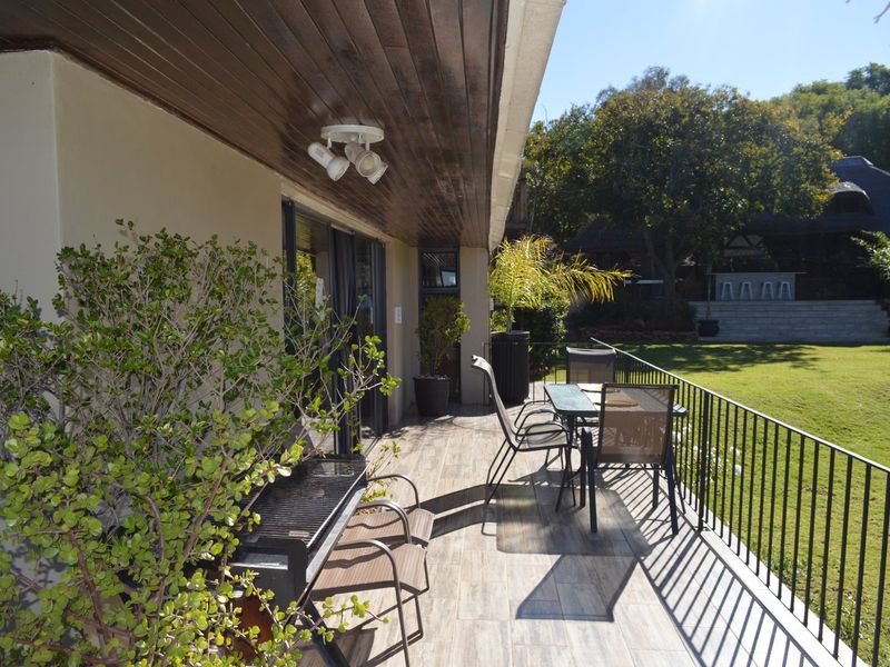 A spacious covered patio featuring tiled flooring, a timber-clad ceiling, and metal railings, overlooking a well-maintained garden area.