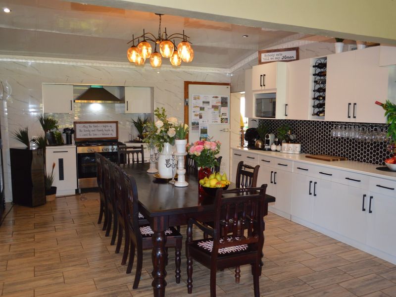 Spacious open-plan kitchen and dining area featuring modern white cabinetry, a gas stove with extractor, tiled flooring, and a dedicated wine storage rack.