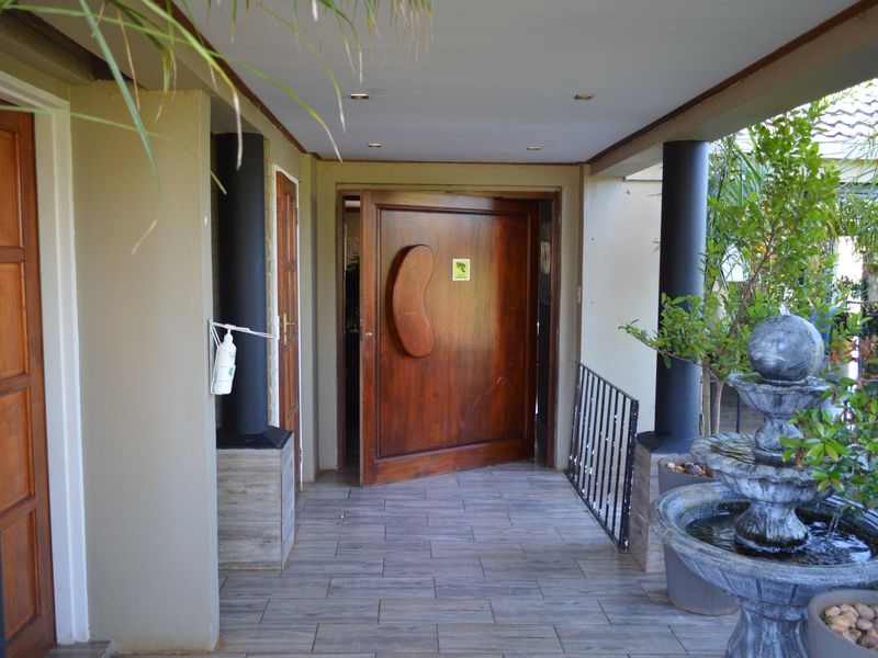 A covered entrance area featuring tiled flooring, stone-clad pillars, and a large wooden pivot door, providing a welcoming and secure access point.