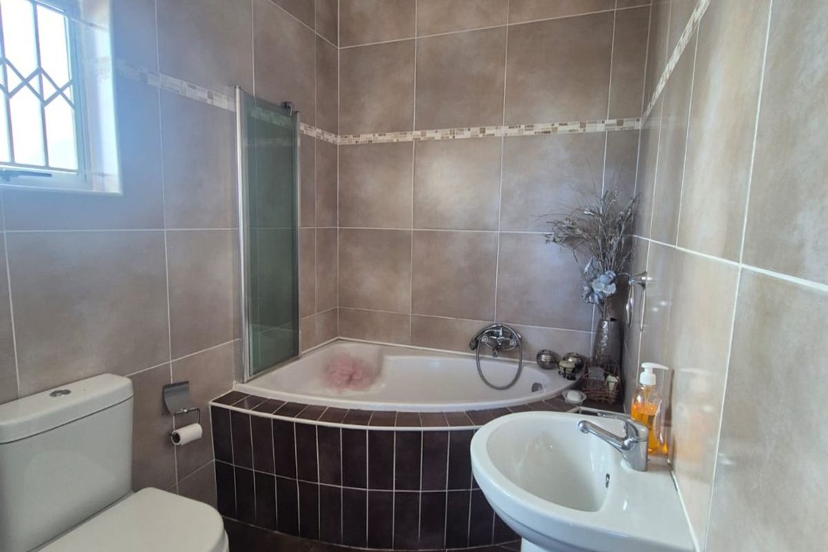 A functional bathroom featuring a corner bathtub, pedestal basin, and toilet, finished with neutral wall and floor tiling.