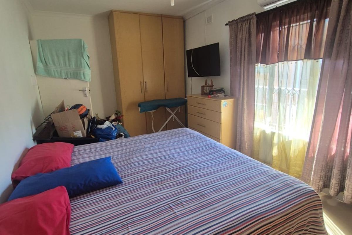 A functional bedroom featuring tiled flooring, a built-in wardrobe, a ceiling fan, and a wall-mounted air conditioning unit.