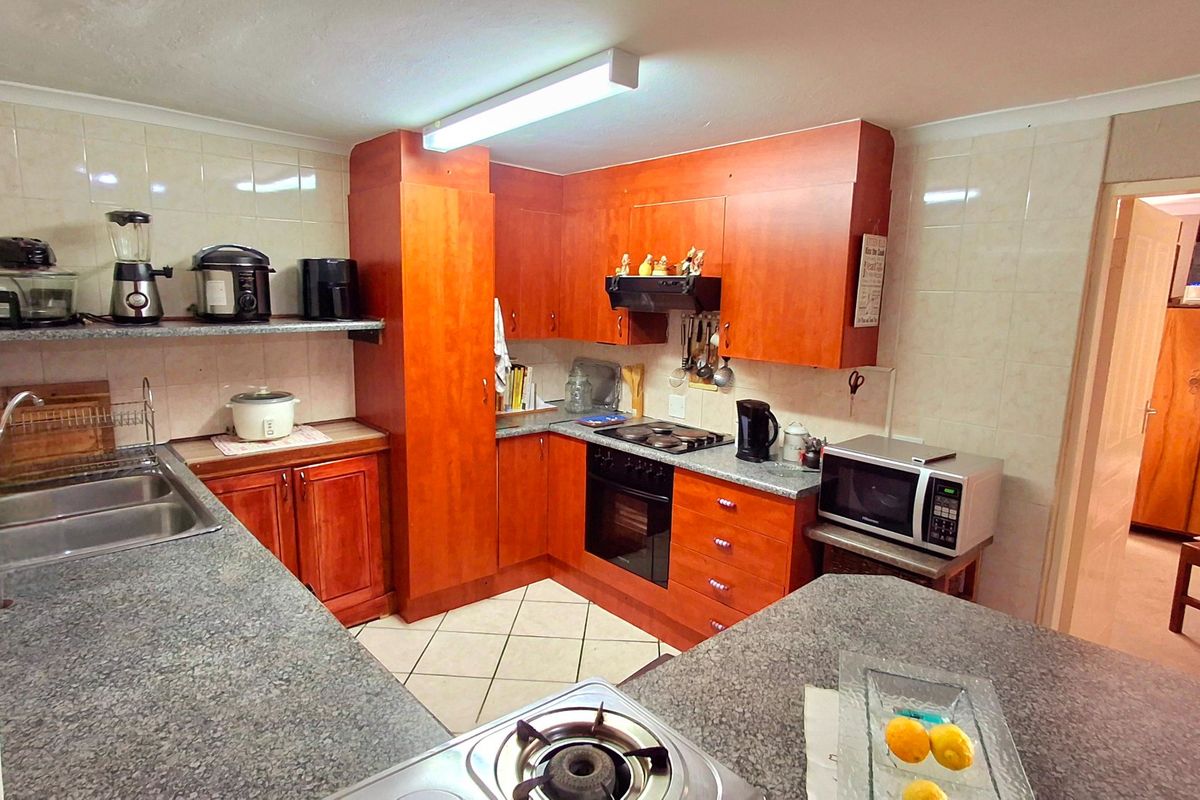 A functional kitchen featuring wood-look laminate cabinetry, granite countertops, built-in oven, hob, and extractor fan with tiled splashbacks and flooring.