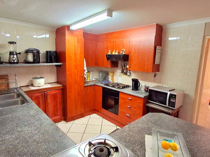 A functional kitchen featuring wood-look laminate cabinetry, granite countertops, built-in oven, hob, and extractor fan with tiled splashbacks and flooring.
