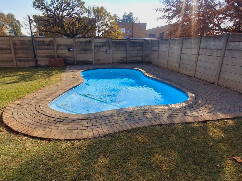 A private backyard featuring a swimming pool surrounded by brick paving and enclosed by a precast concrete boundary wall.