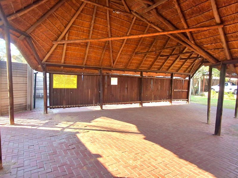 A covered outdoor patio area featuring a traditional thatch roof, timber support structures, and durable brick paver flooring.