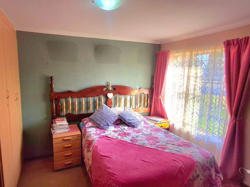 A bedroom featuring built-in wardrobes and a window with security gate, requiring cosmetic updates to the wall finishes.