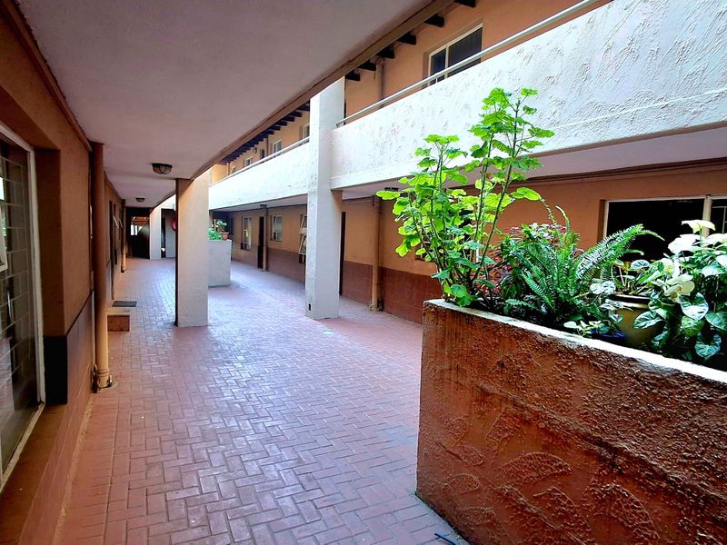 An open-air apartment complex hallway featuring brick paving, concrete structural pillars, and a built-in planter box.