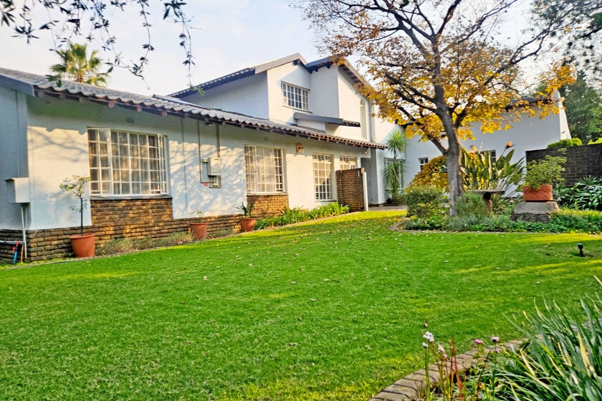 A well-maintained rear garden view featuring a lush green lawn, established trees, and the rear elevation of the house with brick and plaster finishes.