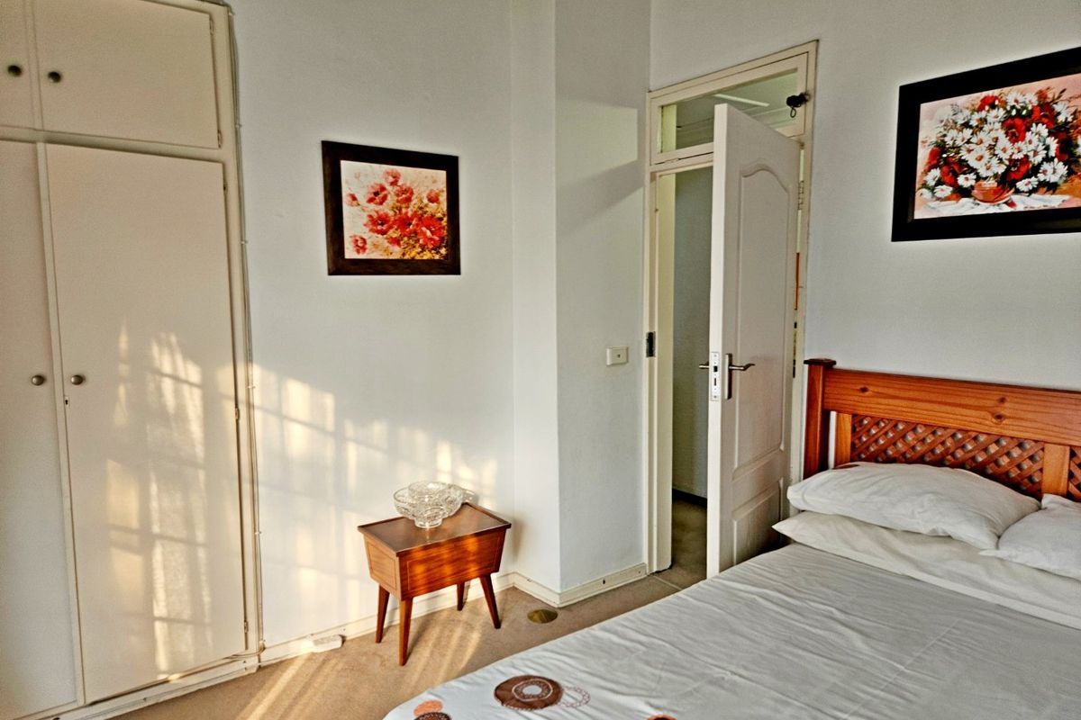 A functional bedroom featuring built-in wardrobe storage, carpeted flooring, and direct access to an adjoining room.