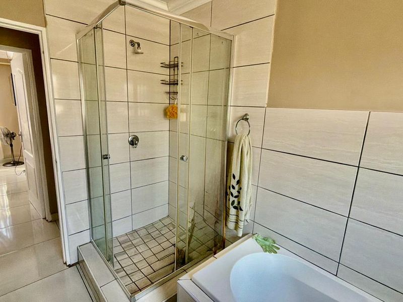 A functional bathroom featuring a glass-enclosed shower, tiled walls, and a built-in bathtub, providing a clean and practical layout.
