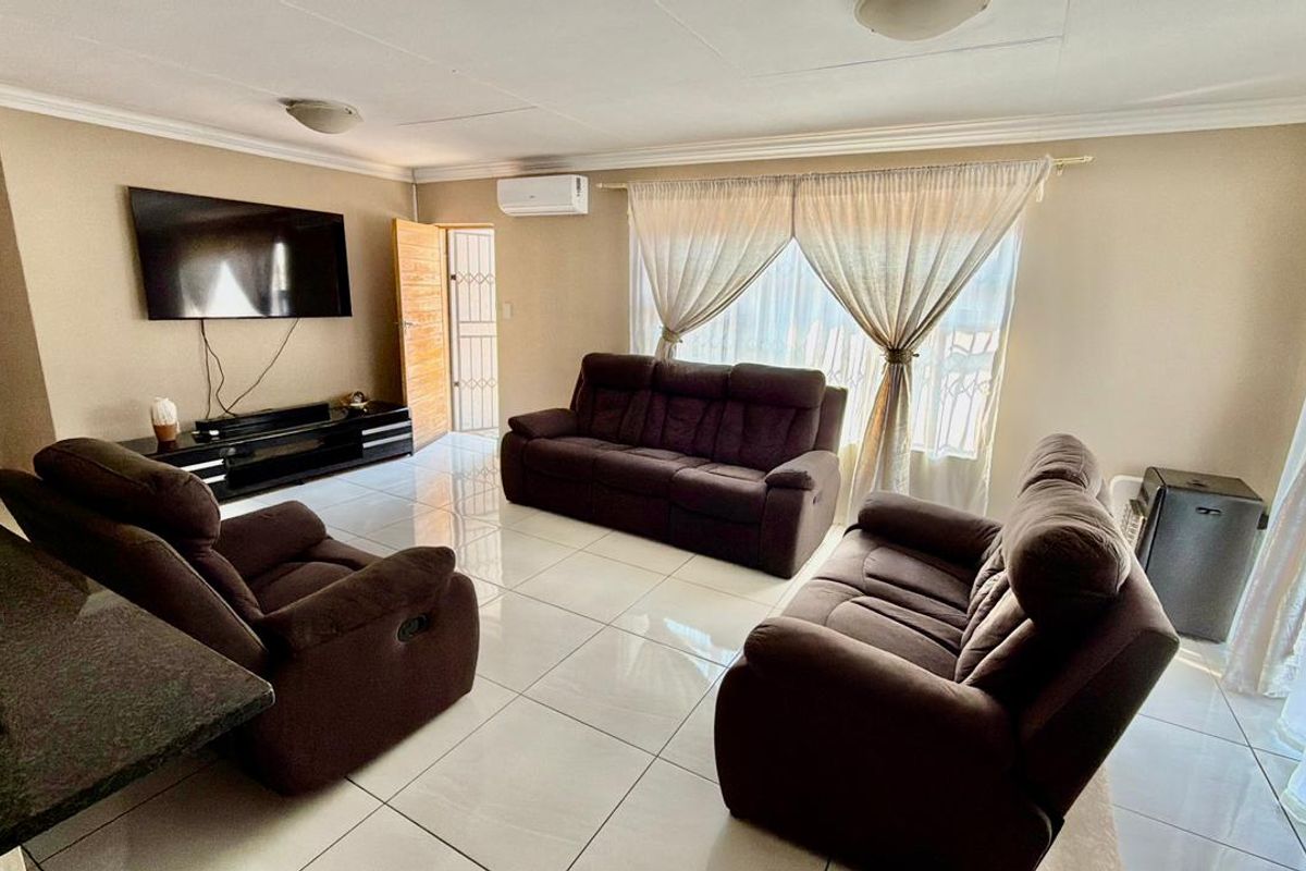 A bright living room featuring large format floor tiles, coved ceilings, and a wall-mounted air conditioning unit.