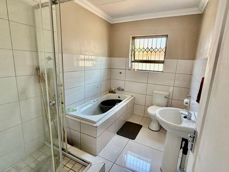 A functional bathroom featuring a tiled shower enclosure, built-in bathtub, pedestal basin, and toilet, with security bars fitted to the window.